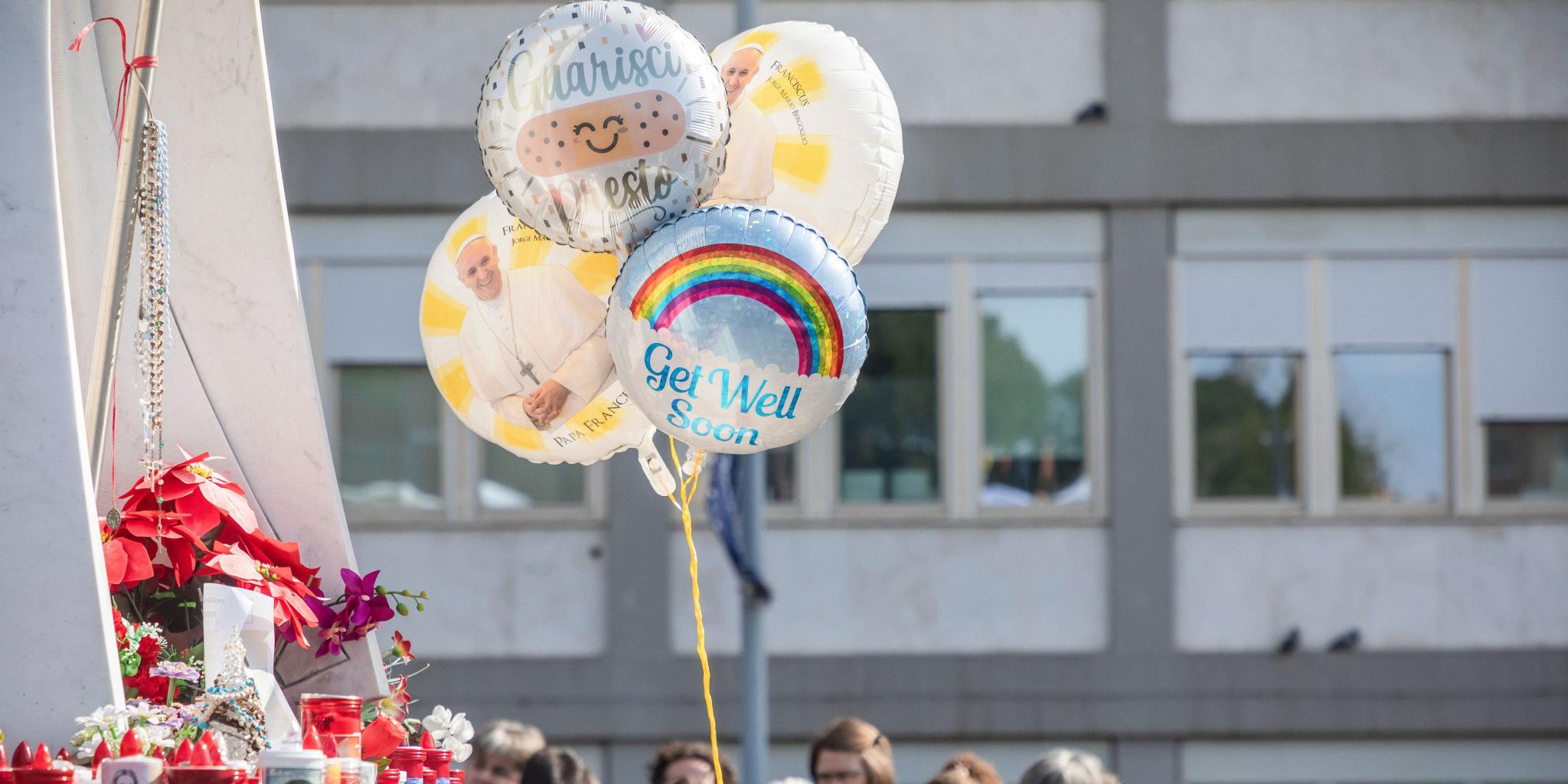 Menschen mit Votivkerzen, Luftballons, Glückwunschkarten und Blumen vor dem Gemelli-Krankenhaus beten für den kranken Papst Franziskus.