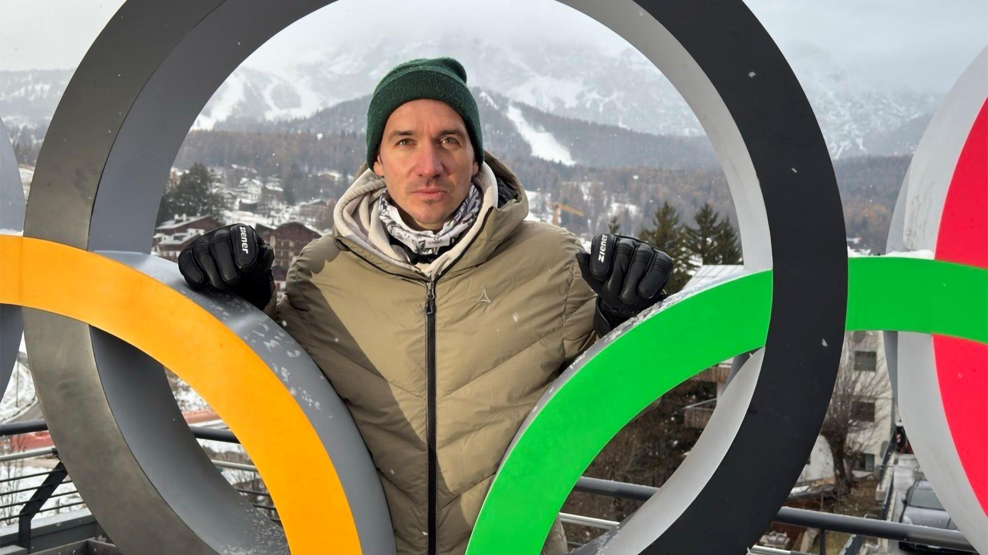 ein Mann schaut durch einen der Ringe einer Figur der Olypmpischen Ringe